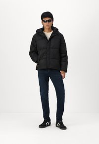 Black puffer jacket with a hood, featuring a quilted design. Paired with dark jeans and black sneakers with white stripes.