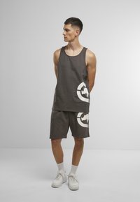 Dark gray tank top and shorts set made of cotton, featuring a large white graphic design on both pieces. Finished with white sneakers.