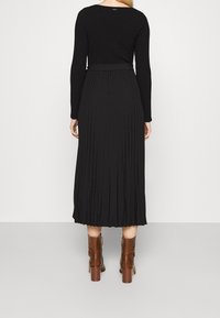 Sort ribbet langærmet top parret med en plisseret sort midi-nederdel. Modellen har brune strukturerede ankelstøvler med blokhæle på.