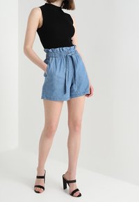 Ljusblå denimshorts med resårmidja och knytbälte, kombinerade med en figurnära svart ärmlös topp och svarta högklackade sandaler.