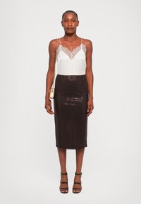 Donna che indossa una canotta con pizzo bianco, una gonna midi scura con paillettes, tacchi a strappo neri e una piccola borsa dorata a spalla, in piedi contro uno sfondo bianco.