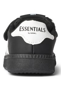 Sort og hvid sneaker med en tekstureret gummisål, tykk sort hæl og "ESSENTIALS by AANKL" logoet tydeligt vist bagpå.