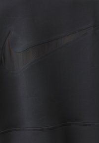 Top sportivo nero con un tessuto liscio e elasticizzato, caratterizzato da un dettaglio trasparente a taglio sul lato sinistro e una cucitura nella parte inferiore.
