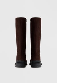 Rudos zomšinės ilgaauliai batai iki kelio su matinio paviršiaus apdaila, juodu guminiu padu ir užtrauktuku gale.