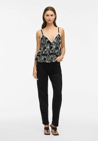 Top peplum floreale nero con spalline sottili, caratterizzato da un profondo scollo a V e un motivo floreale bianco contornato. Abbinato a pantaloni neri e sandali.