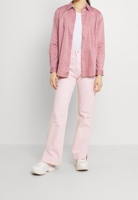 Light pink button-up shirt paired with matching pink flared pants and white sneakers. Smooth fabric with a collar and long sleeves.