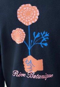 Materialul naval are un desen cu două flori roz stilizate, ținute de o mână în bej deschis. Textul „Rêve Botanique” este scris cu un font roz dedesubt.