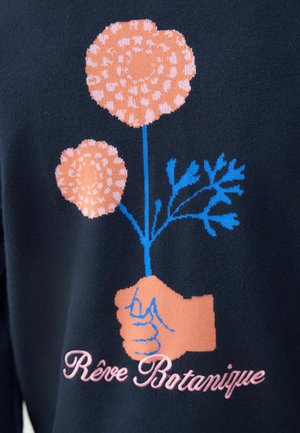 Marineblauer Stoff zeigt eine Grafik von zwei stilisierten rosa Blumen, die von einer Hand in hellem Beige gehalten werden. "Rêve Botanique" steht darunter in rosafarbener Schrift.