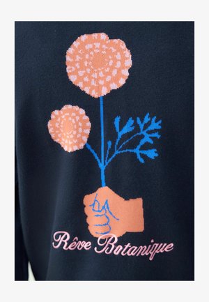 Granatowa tkanina zdobi graficzny motyw dwóch stylizowanych różowych kwiatów trzymanych przez dłoń w jasnobeżowym odcieniu. Poniżej różowym pismem odręcznym widnieje napis "Rêve Botanique".