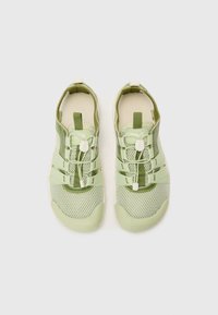 Adidași de culoare verde deschis, cu uppers din plasă și material sintetic, având șireturi elastice și o talpă din cauciuc texturat pentru aderență.