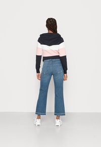 Sweatshirt com capuz em riscas azul, rosa e branca; combinado com jeans azuis de cintura alta e pernas largas; ténis brancos visíveis.