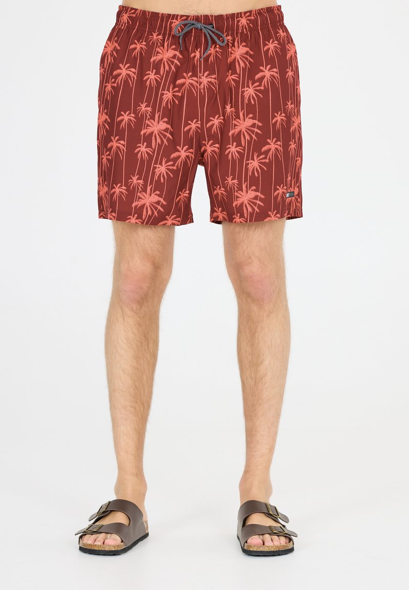 Röda simshorts med palmmönster. Tillverkade av lätt tyg, de har resårmidja och snörning, tillsammans med bruna sandaler.