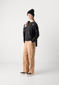 Felpa nera con dettagli ricamati multicolori, pantaloni cargo beige, berretto nero e sneaker nere con suola bianca.