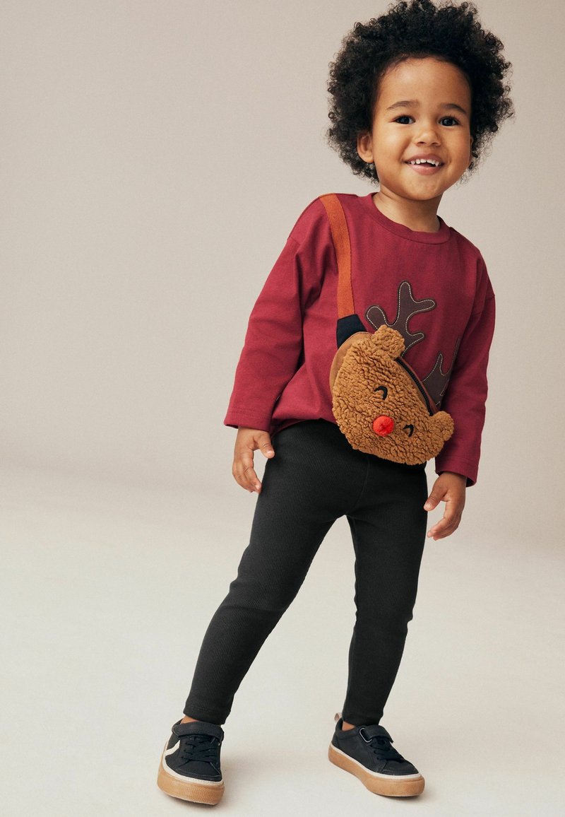 Chemise à manches longues bordeaux avec un motif de renne, pantalon noir côtelé, et un sac bandoulière en peluche marron. Baskets noires avec semelles brunes.