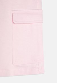 Vêtement en coton rose clair avec un détail de poche, présentant des lignes épurées, une texture lisse et des coutures soignées le long de l'ourlet et des bords.