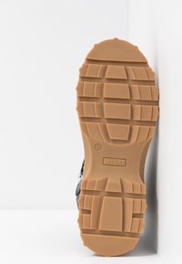 Černá podrážka boty s texturovaným gumovým gripem, která má mohutný vzor a světle hnědou podrážku. Na spodní straně je velikost 37 a značka "MONKL".