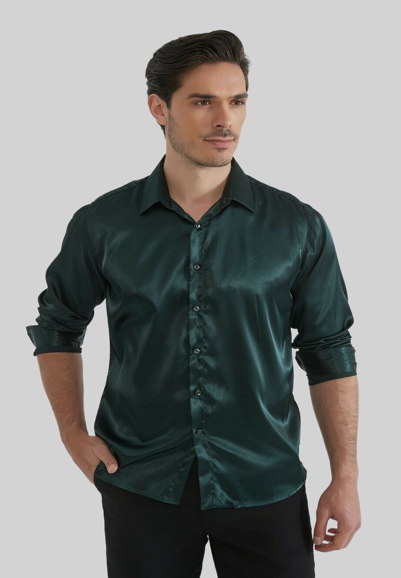 Chemise en satin vert foncé avec un design à boutons, manches longues retroussées, texture brillante et col standard. Pantalon noir porté avec.