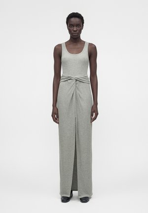 Femeie stând cu fața spre înainte purtând o rochie maxi gri fără mâneci cu detaliu nod în talie și crăpătură frontală, asortată cu pantofi negri.