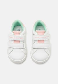Weiße Kindersneaker mit pinken Akzenten, mintgrüner Innensohle, doppeltem Klettverschluss und Tommy Hilfiger-Branding auf weißem Hintergrund.