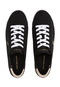 Μαύρα καμβά παπούτσια με λευκά κορδόνια, χρυσές λεπτομέρειες και λευκή ελαστική σόλα. Η ετικέτα στο εσωτερικό γράφει "TOMMY HILFIGER" με χρυσά γράμματα.