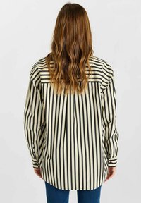 Zwart en crèmekleurig gestreepte shirt, losse pasvorm, met lange mouwen en een ronde zoom. De achterkant heeft een yoke en plooi-details voor extra structuur.