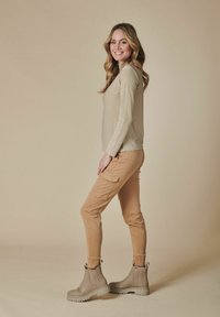 Beige Langarmtop mit einem subtilen Glitzer, kombiniert mit beigen Cargo-Hosen und hellgrauen Knöchelstiefeln mit strukturiertem Profil und elastischen Seiten.