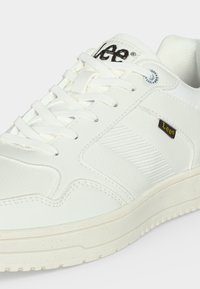 Baskets blanches à lacets avec panneau latéral texturé, col rembourré et petite étiquette de logo "Lee" noire et jaune sur le côté extérieur.