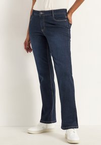 Mörkblå denimjeans med rak benpassform, synliga fickor och kontrasterande sömmar. Kombineras med vita sneakers och en enkel topp.