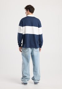 Navy and white long-sleeve polo shirt with a relaxed fit, featuring horizontal stripes and ribbed cuffs, paired with light blue straight-leg jeans.