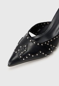 Black pointed-toe leather shoe with silver stud embellishments and a curved strap detail across the front.