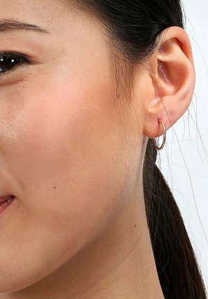 Orecchino a cerchio dorato all'orecchio di un modello, caratterizzato da un design sottile e rotondo con una texture liscia. L'orecchino è piccolo e minimalista.