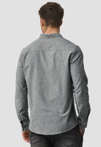 Gray long-sleeve shirt made from a textured fabric, featuring a button-down collar and single button cuffs, with a curved hem.
