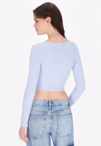 Top scurt cu maneci lungi, de culoare albastru deschis, cu un gât rotund. Purtați cu blugi din denim cu talie înaltă, decolorati, cu buzunare din material. 