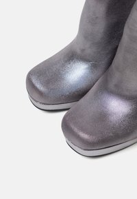Metalliset hopeiset nilkkurit, joissa on sileä pinta, pyöreä varvas ja huomaamaton uurrettu rakenne, varustettuna tasaisella korolla ja tyylikkäällä muotoilulla.