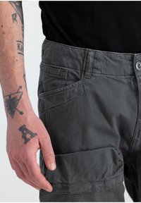 Pantalones cargo de algodón gris con bolsillos laterales, costuras visibles y cierre de botón. La textura parece robusta, adecuada para el uso casual.