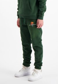 Groene katoenen sweatpants hebben een basketbalgrafiek en logo, met een elastische tailleband en boorden, gecombineerd met witte sneakers.