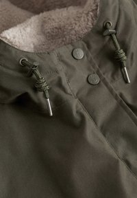 Khaki takki, jossa on teksturoitu sisävuori, varustettu nyöri sulkimilla ja yhteensopivilla nappiin. Suora pinta, jossa on ommeltuja yksityiskohtia.