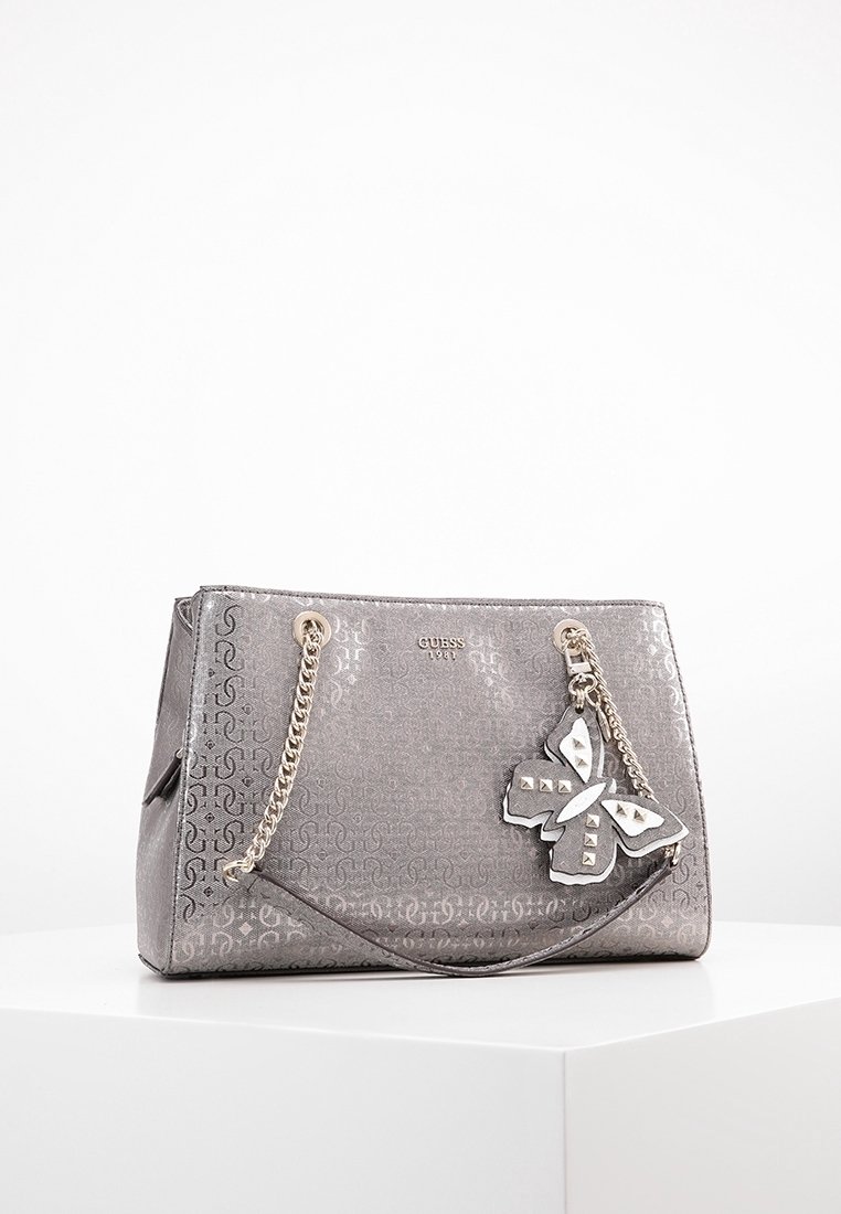 Grijze synthetische handtas met reliëflogo-patroon, zilveren kettingschouderriemen en een decoratieve vlinderaccent. Heeft een gestructureerde vorm.