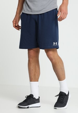 Marinefarbene Sportshorts mit elastischem Bund und weißem Under Armour-Logo. Getragen mit einem grauen Shirt, schwarzen Sneakers und weißen Kniestrümpfen.