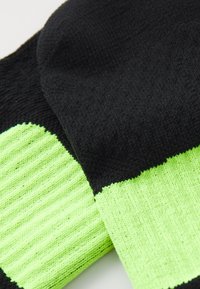 Schwarze und neon grüne gestrickte Socken mit gerippten neon grünen Bündchen, die übereinander auf einer weißen Fläche liegen.
