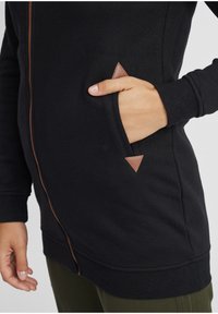Felpa nera con zip realizzata in tessuto morbido, dotata di una tasca laterale con un accento triangolare marrone e polsini e orlo a costine.