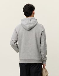 Γκρι φούτερ από βαμβάκι με κουκούλα που ρυθμίζεται με κορδόνι, ριμπ μανίκια και μέση. Φορεμένο ανάποδα, αναδεικνύει έναν απλό σχεδιασμό και χαλαρή εφαρμογή.