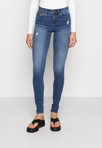 Jeans skinny de cor azul clara com detalhes rasgados. Tecido de denim de algodão, design de cintura alta, combinados com sandálias plataforma pretas.