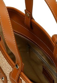 Brązowa skórzana torba tote o plecionej fakturze, z dwoma solidnymi uchwytami, kieszenią na zamek błyskawiczny wewnątrz oraz beżową podszewką.