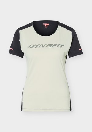 Αθλητική μπλούζα με κοντά μανίκια, ανοιχτόχρωμο μπροστινό μέρος, μαύρα μανίκια, πλευρικά πάνελ και λογότυπο "DYNAFIT" στο στήθος με μαύρο κείμενο.