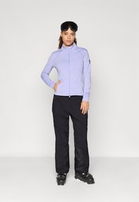 Svetlofialová, dlhá bunda s rukávmi, vysoko golierom, skombinovaná s čiernymi lyžiarskymi nohavicami a čiernymi lyžiarskymi topánkami, s čístým dizajnom a funkčnými vreckami.