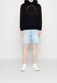 Felpa nera con stampa logo rossa e grigia, abbinata a pantaloni corto in denim azzurri. Sneakers bianche completano l'outfit.