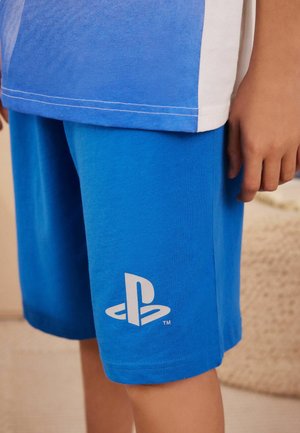 Blå bomullsshorts med en mjuk textur, med en vit PlayStation-logotyp på vänster ben. Knälängd, avslappnad design.