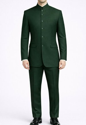 Homme portant un costume col officier vert foncé boutonné, avec un pantalon assorti et des chaussures habillées noires, debout devant un fond blanc uni.