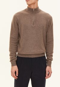 Maglione marrone a maglia con colletto a mezza zip, polsini e orlo a coste, caratterizzato da una texture morbida. Abbinato a pantaloni blu navy, il modello sta in posizione eretta.